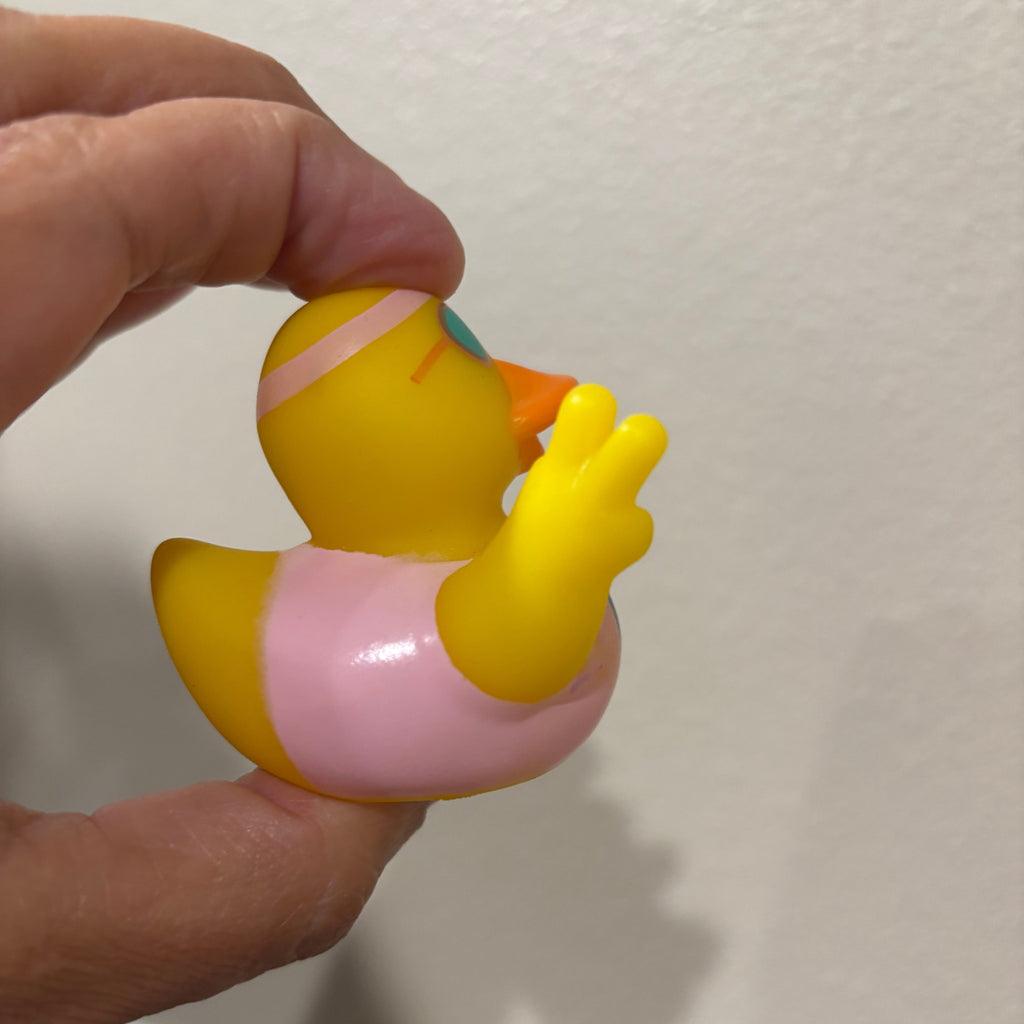 Hand holding a small yellow and pink rubber duck against a plain background