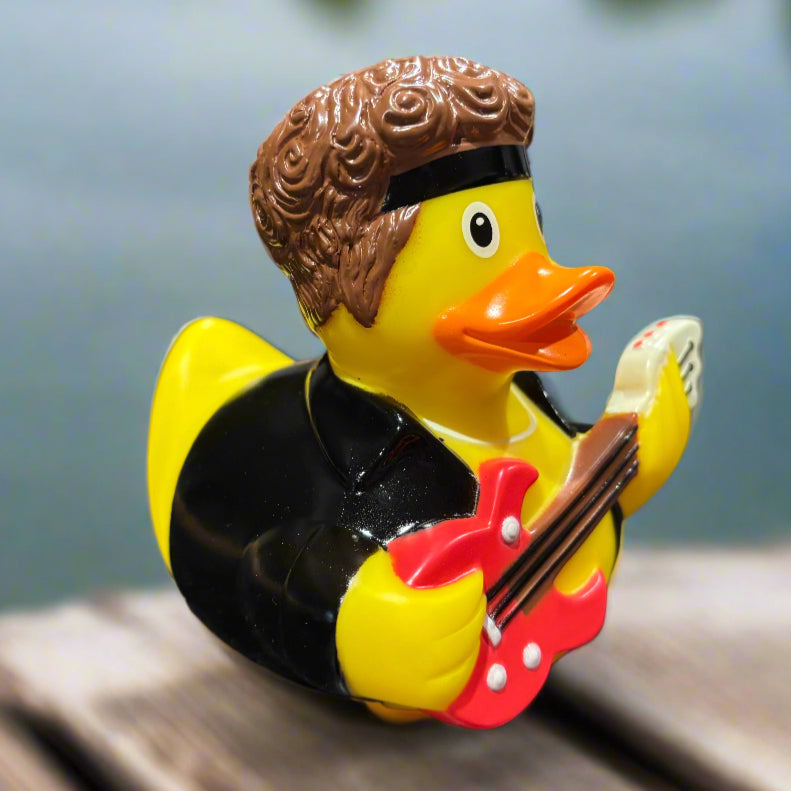 Rubber duck playing a guitar on a dark surface with a blurred background.