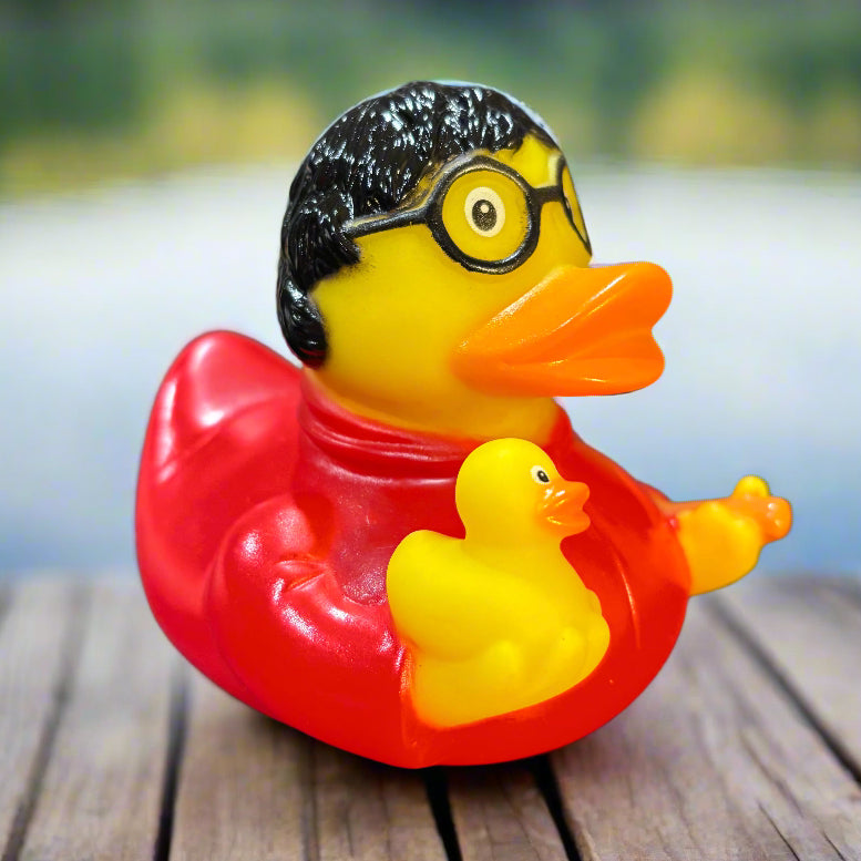 Two small rubber duck toys, one yellow and black, the other red and yellow, on a dark surface with a blurred background.