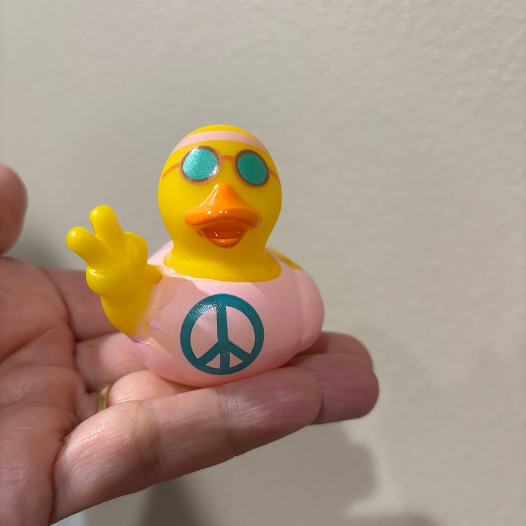 Small yellow duck figurine with a peace symbol on a finger against a neutral background