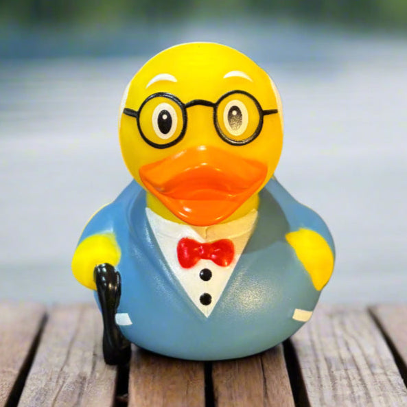 Rubber duck wearing glasses and a suit standing on wooden planks with a blurred water background
