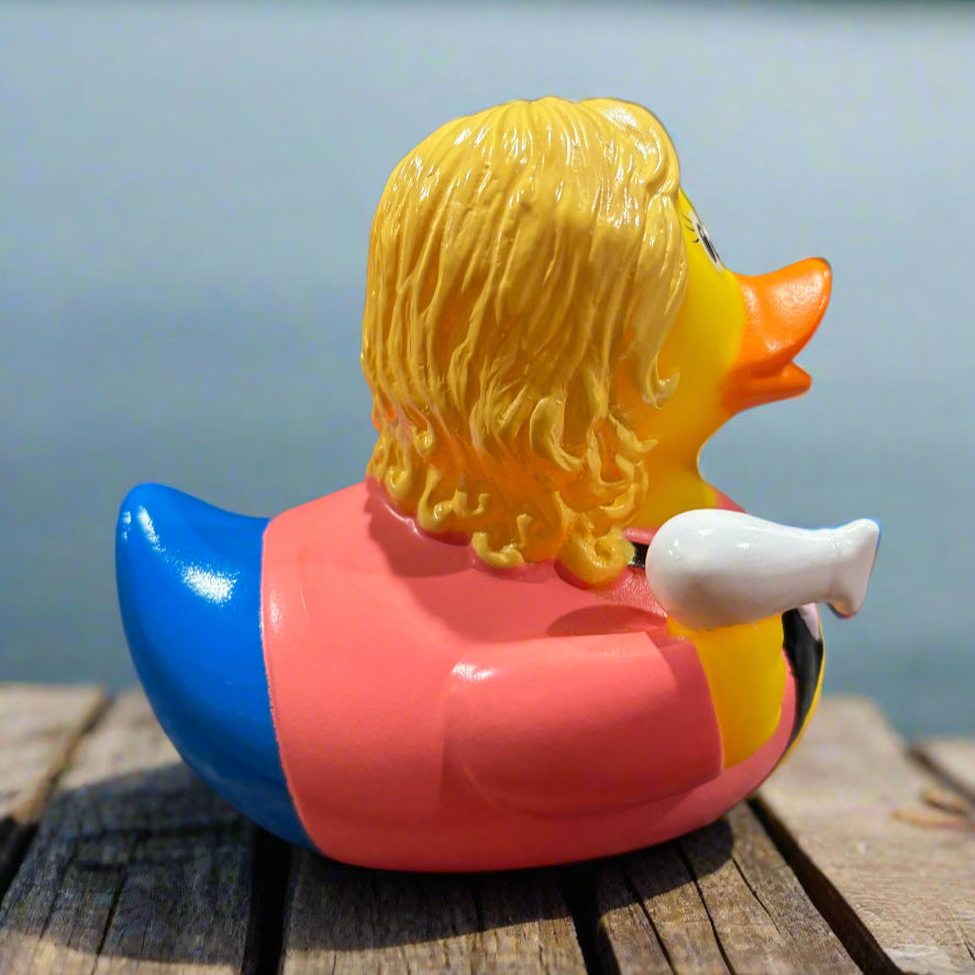 Rubber duck with blonde hair and a pink jacket on a wooden surface with a blue background