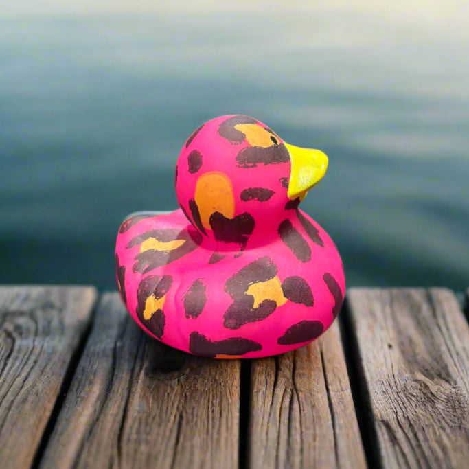 Pink and yellow leopard print rubber duck on a dark surface with a blurred background of similar items.