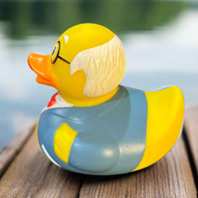 Rubber duck with glasses and a sweater on a wooden dock by a body of water.