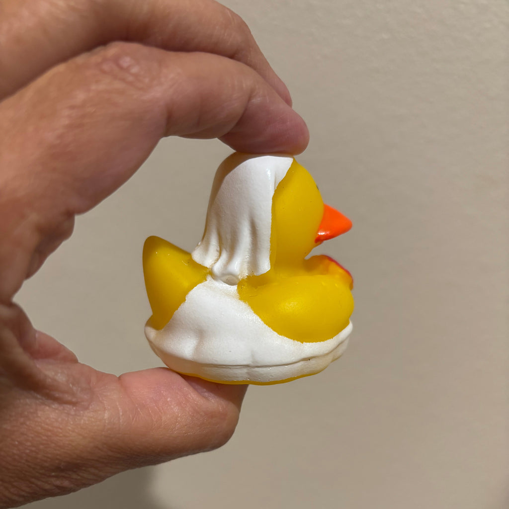 Hand holding a small rubber duck toy against a plain background