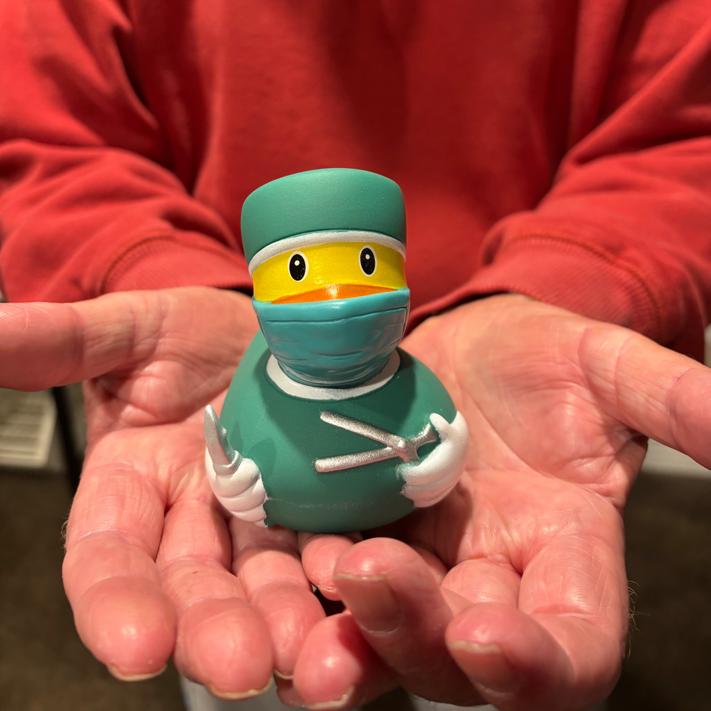 Person holding a teal rubber duck dressed as a medical professional with a face mask.