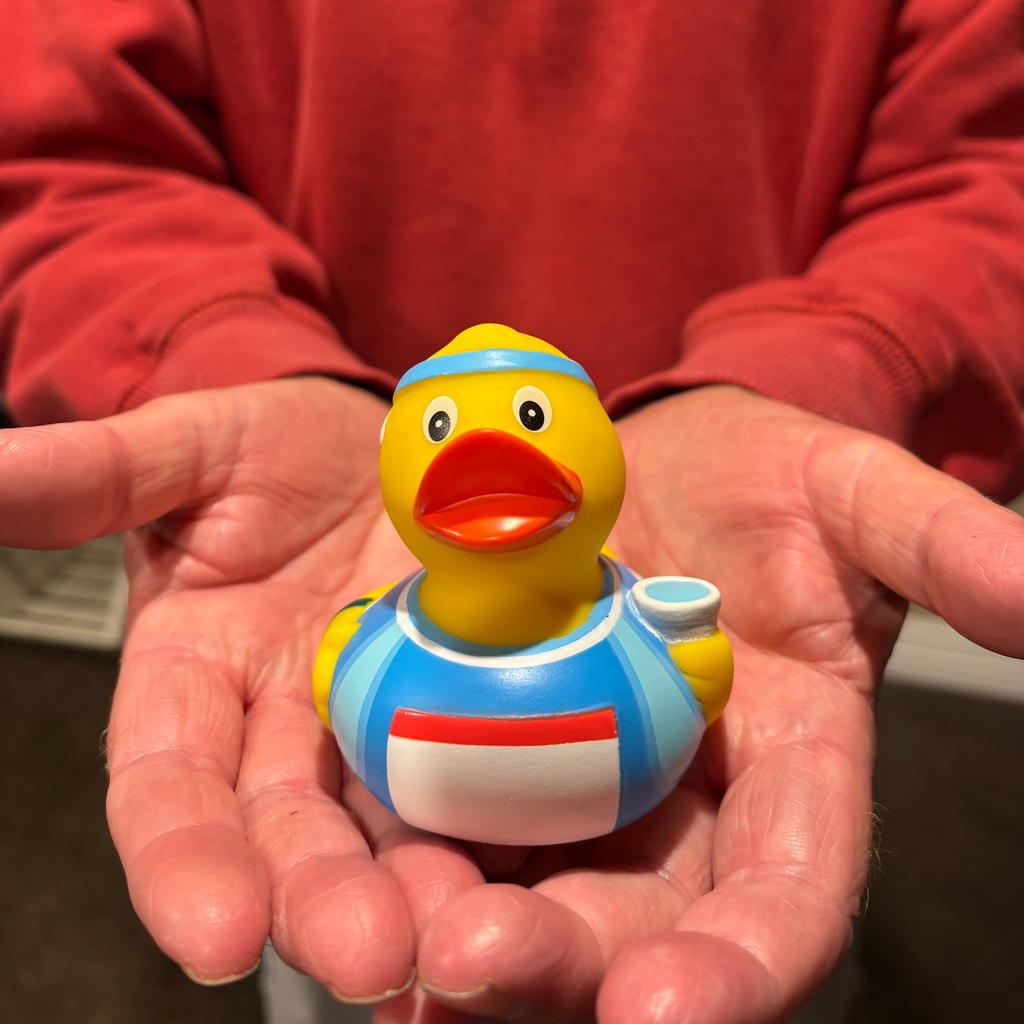 Person holding a small rubber duck toy with a red shirt on a blurred background