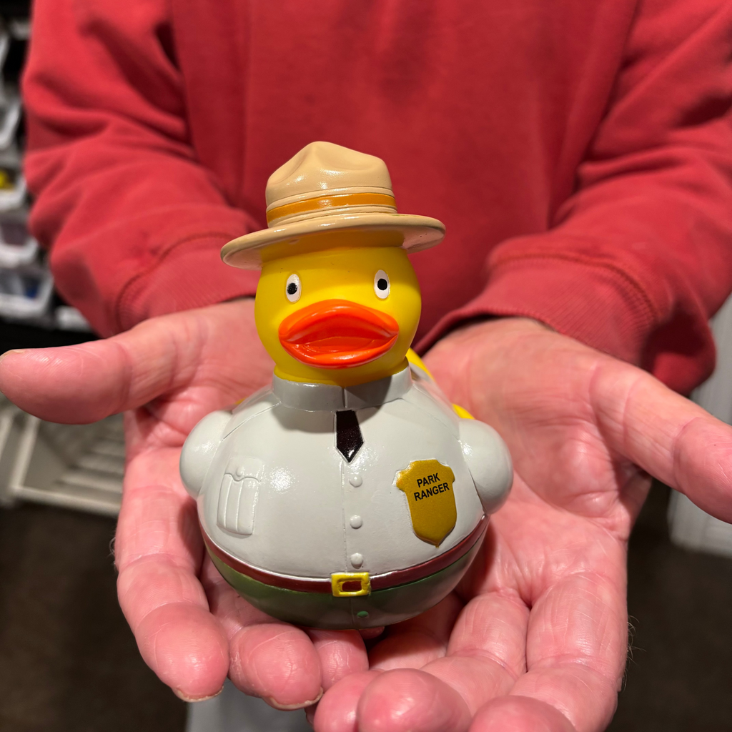 Person holding a rubber duck dressed as a park ranger with a red shirt in the background