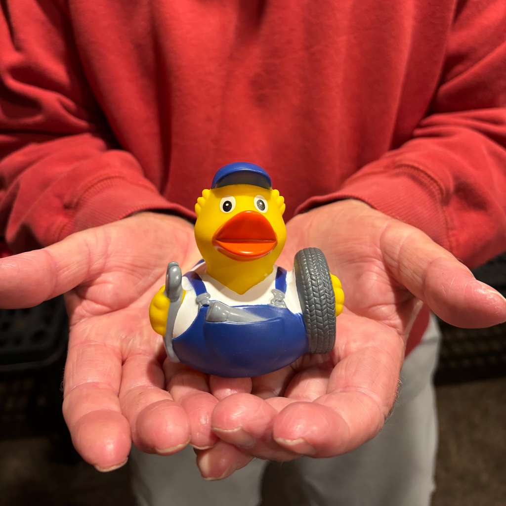 Person holding a small rubber duck toy with a blue cap and overalls.