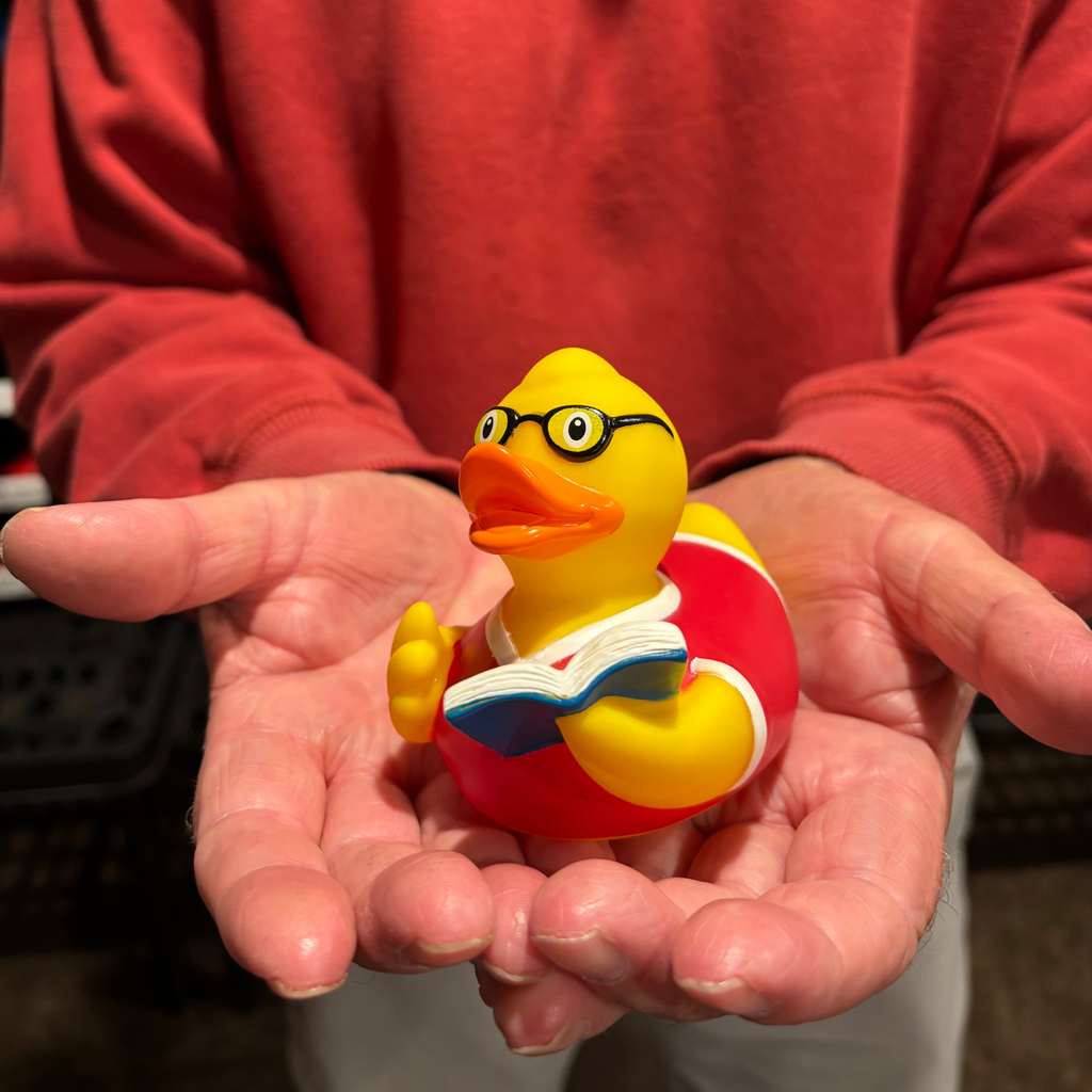 Person holding a rubber duck wearing glasses and reading a book