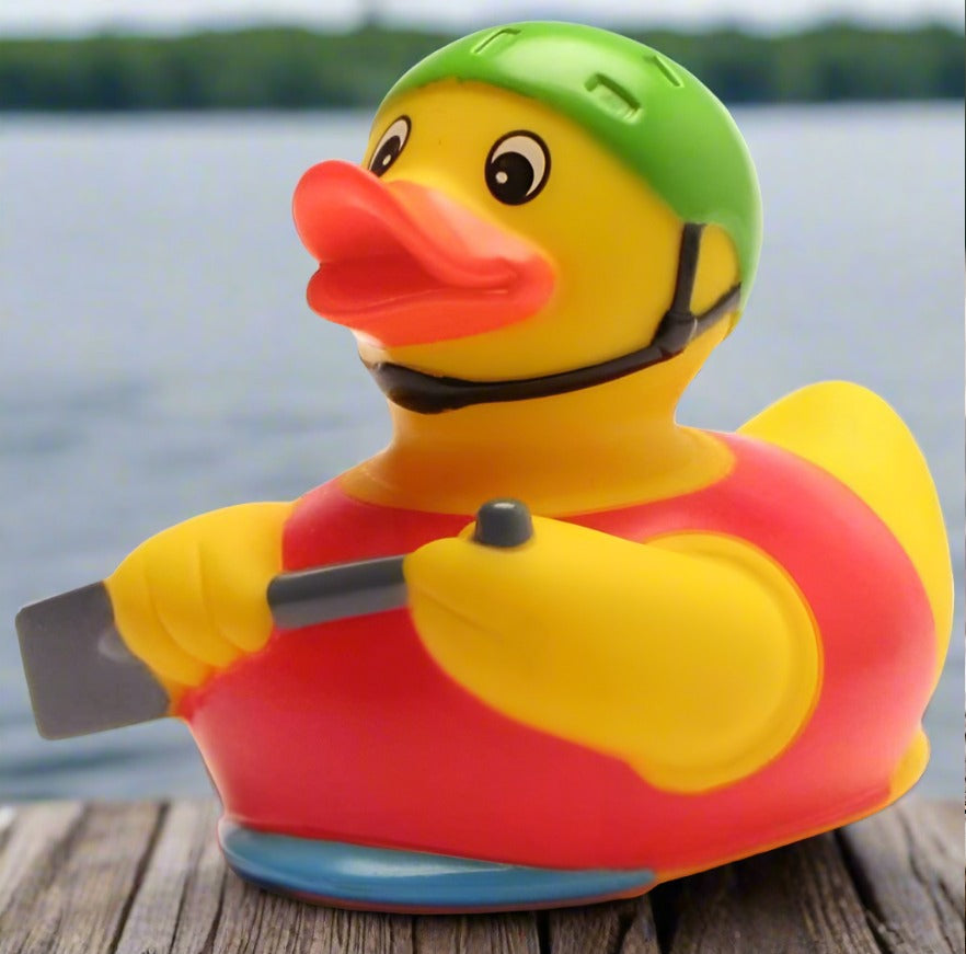 A multicolored rubber duck designed to resemble a cheerful duck wearing a green helmet, with a red shirt and a yellow bill, positioned on a flat surface, likely a car dashboard.